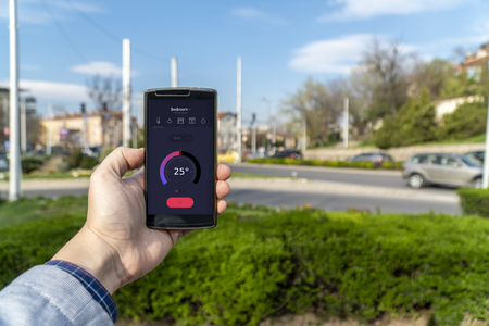 Home automation and smart home concept. Human nad holding a smartphone on the street and adjusting...