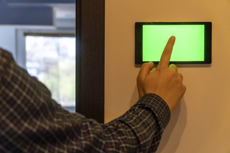 Smart home control and security concept. Device with blank screen hanging on a wall and person pressing button with his finger.の写真素材
