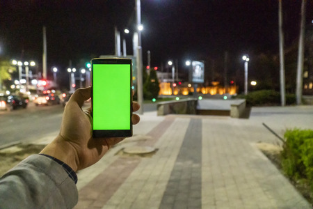 Home automation and smart home concept. Human nad holding a smartphone on the street at night and adjusting the home temperature from an app.の写真素材