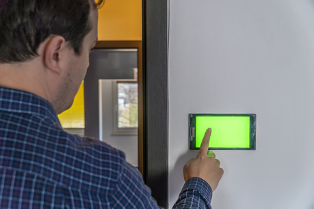 Smart home control and security concept. Device with blank screen hanging on a wall and person pressing button with his finger.の写真素材