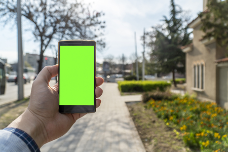 Person holding smartphone with blank screen with city streets in the backgroundの写真素材