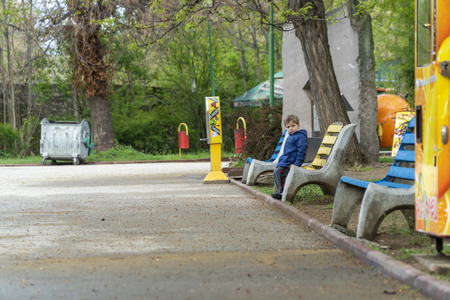 Young boy sitting on a bench alone and waiting for someone to find himの写真素材
