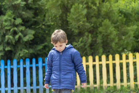 Yound boy walking around in a park with his head down with a colorful fence in the backgroundの写真素材