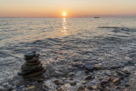 Stack of rock on the beach during sunset, with a boat in the background. Zen mood concept.の写真素材