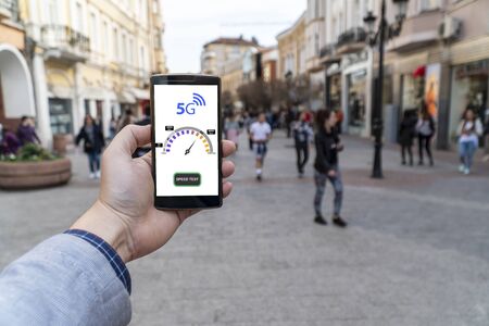 5g network street speed test. Man holding a smartphone outside and checking the 5g speed.