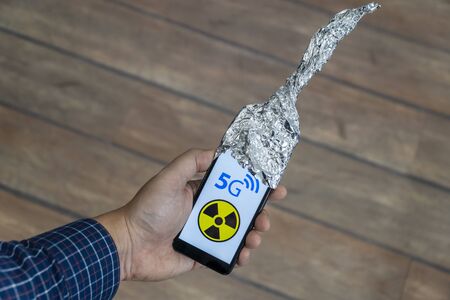 5g network danger concept. Smartphone with antenna made out of aluminum foil to block the signal. Danger sign is displayed on the phone.の写真素材