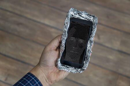 5g network danger concept. Smartphone with protective case made out of aluminum foil to block the signal. Danger sign is displayed on the phone.の写真素材