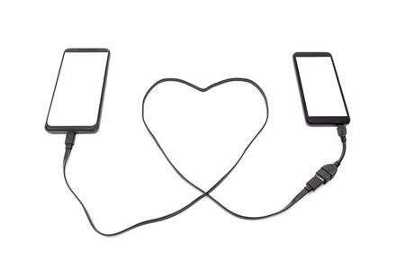 Hand connecting two smartphones with a heart shaped USB cable. Long distance relationship concept.の写真素材