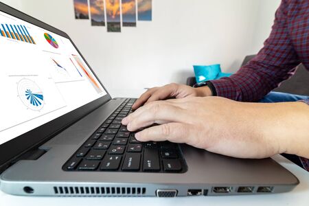 Working from home concept. Man looking at business intelligence charts on a laptop at home.の写真素材
