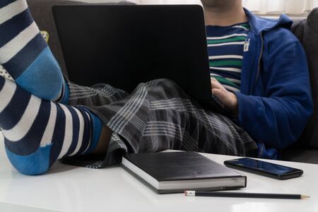 Work from home concept. Man dressed in a hoody and pijamas having a conference call on a bed with a laptop.の写真素材