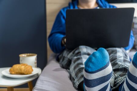 Work from home concept. Man dressed in a hoody and pijamas having a conference call on a bed with a laptop.の写真素材