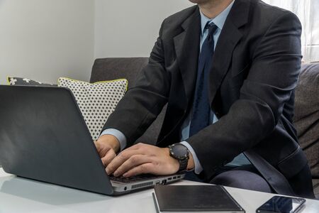 Work from home concept. Businessman dressed in a suit having a conference call on a couch with a laptop.の写真素材