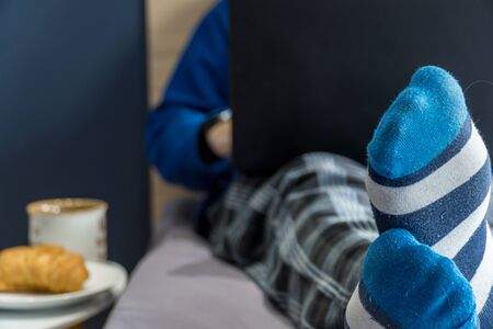 Work from home concept. Man dressed in a hoody and pijamas having a conference call on a bed with a laptop.の写真素材