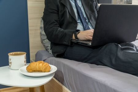 Work from home concept. Businessman dressed in a suit having a conference call on a bed with a laptop.の写真素材