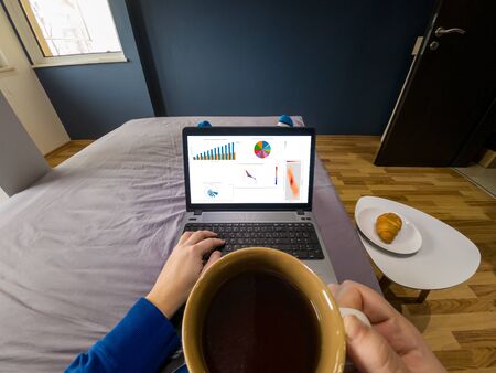 Work from home concept. POV view of a drinking coffee in bed with a laptop.の写真素材