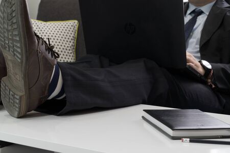 Work from home concept. Businessman dressed in a suit having a conference call with is legs up on a coffee table.の写真素材