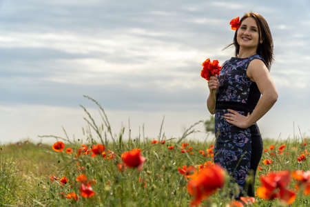 A young woman in a blue dress in a poppy flower field with beautiful clouds in the backgroundの写真素材