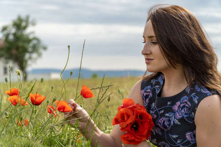 A young woman in a blue dress in a poppy flower field with beautiful clouds in the backgroundの写真素材