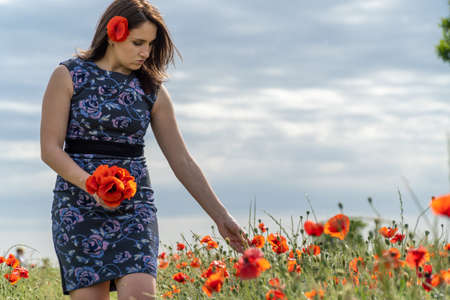 A young woman in a blue dress in a poppy flower field with beautiful clouds in the backgroundの写真素材