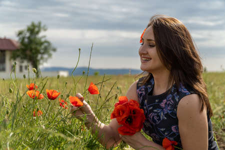 A young woman in a blue dress in a poppy flower field with beautiful clouds in the backgroundの写真素材