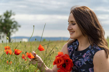 A young woman in a blue dress in a poppy flower field with beautiful clouds in the backgroundの写真素材