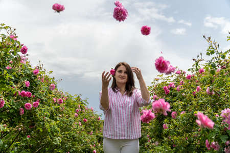 Young woman throwing Bulgarian pink roses in a garden with beautiful clouds in the backgroundの写真素材