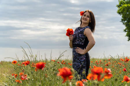 A young woman in a blue dress in a poppy flower field with beautiful clouds in the backgroundの写真素材