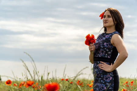 A young woman in a blue dress in a poppy flower field with beautiful clouds in the backgroundの写真素材