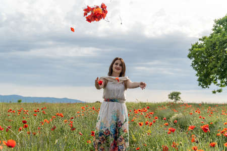 Young woman in a white dress throwing red poppy flowers at the cameraの写真素材