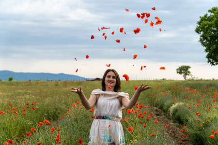 Young woman in a white dress throwing red poppy flowers at the cameraの写真素材