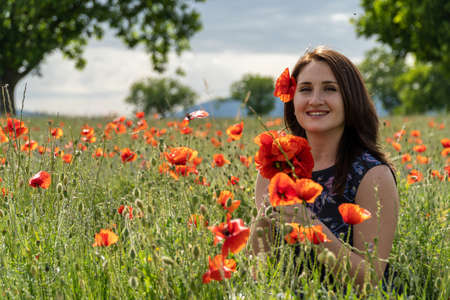 A young woman in a blue dress in a poppy flower field with beautiful clouds in the backgroundの写真素材