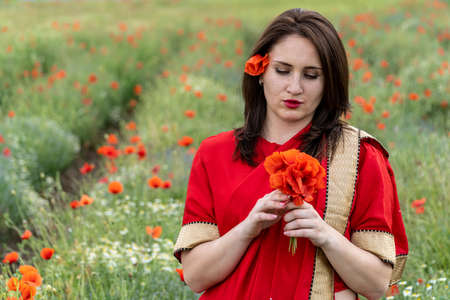 Young woman dressed in a traditional Indian costume called Sari walking in a red poppy flower fieldの写真素材