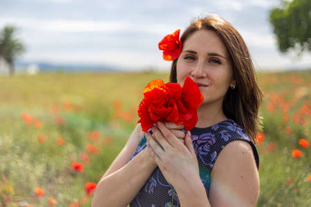 A young woman in a blue dress in a poppy flower field with beautiful clouds in the backgroundの写真素材
