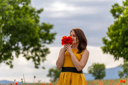 A young woman in a yellow dress in a poppy flower field with beautiful clouds in the backgroundの写真素材