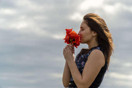 A young woman in a blue dress in a poppy flower field with beautiful clouds in the backgroundの写真素材