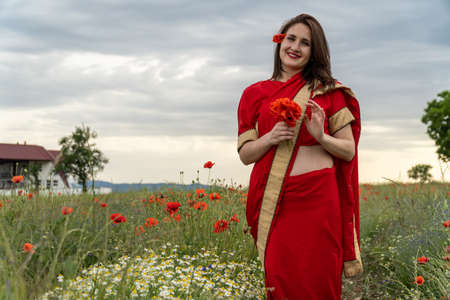 Young woman dressed in a traditional Indian costume called Sari walking in a red poppy flower fieldの写真素材
