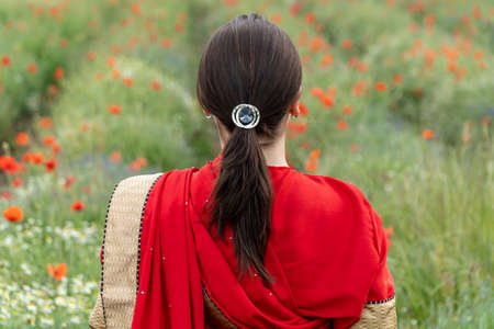 Young woman dressed in a traditional Indian costume called Sari walking in a red poppy flower fieldの写真素材