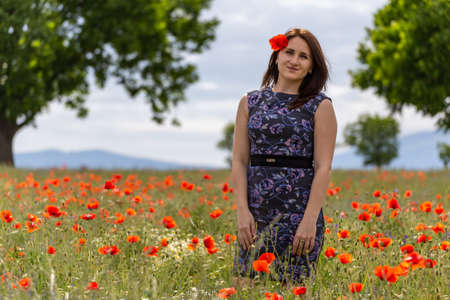 A young woman in a blue dress in a poppy flower field with beautiful clouds in the backgroundの写真素材