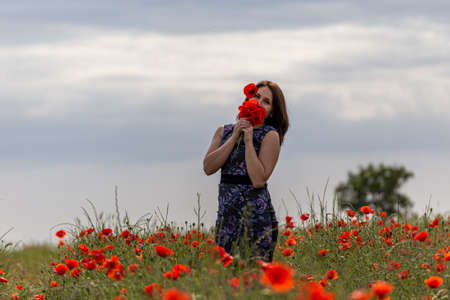 A young woman in a blue dress in a poppy flower field with beautiful clouds in the backgroundの写真素材