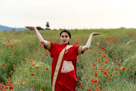 Young woman dressed in a traditional Indian costume called Sari walking in a red poppy flower fieldの写真素材