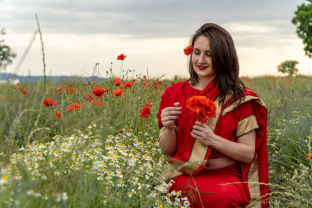 Young woman dressed in a traditional Indian costume called Sari walking in a red poppy flower fieldの写真素材