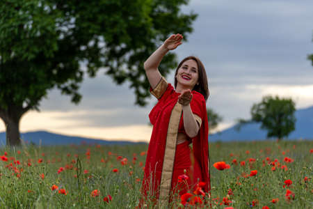 Young woman dressed in a traditional Indian costume called Sari walking in a red poppy flower fieldの写真素材