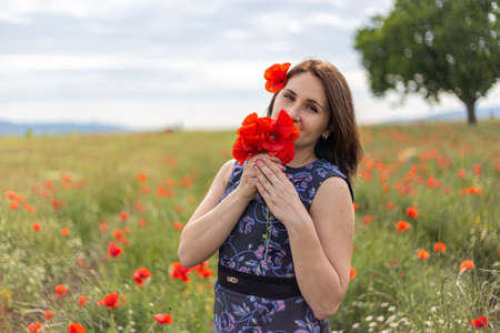A young woman in a blue dress in a poppy flower field with beautiful clouds in the backgroundの写真素材