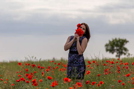 A young woman in a blue dress in a poppy flower field with beautiful clouds in the backgroundの写真素材