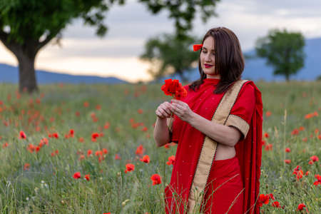 Young woman dressed in a traditional Indian costume called Sari walking in a red poppy flower fieldの写真素材