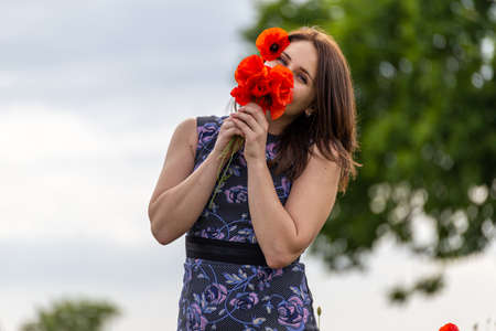 A young woman in a blue dress in a poppy flower field with beautiful clouds in the backgroundの写真素材