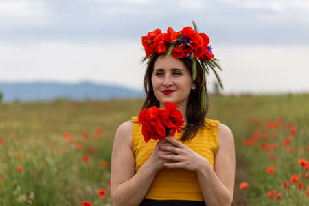 A young woman in a yellow dress in a poppy flower field with beautiful clouds in the backgroundの写真素材