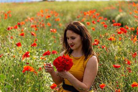 A young woman in a yellow dress in a poppy flower field with beautiful clouds in the backgroundの写真素材
