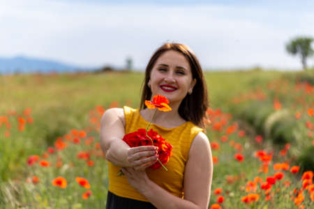 A young woman in a yellow dress in a poppy flower field with beautiful clouds in the backgroundの写真素材