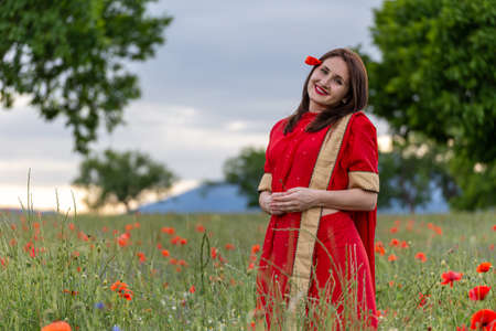 Young woman dressed in a traditional Indian costume called Sari walking in a red poppy flower fieldの写真素材